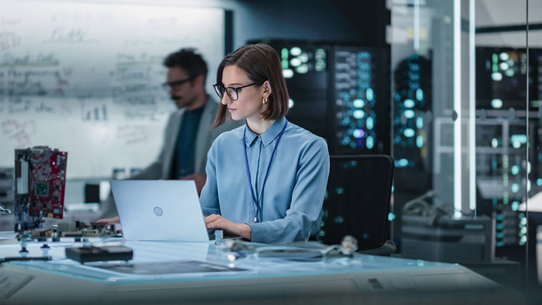 Woman with a headset on looking at dual computer screens.
